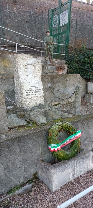 Cippo commemorativo con scultura e corona di alloro, simbolo di ricordo e onore.
