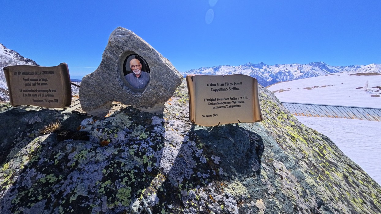 Masso roccioso con ritratto fotografico incassato e targhe in bronzo con iscrizioni, su cresta innevata di montagna.