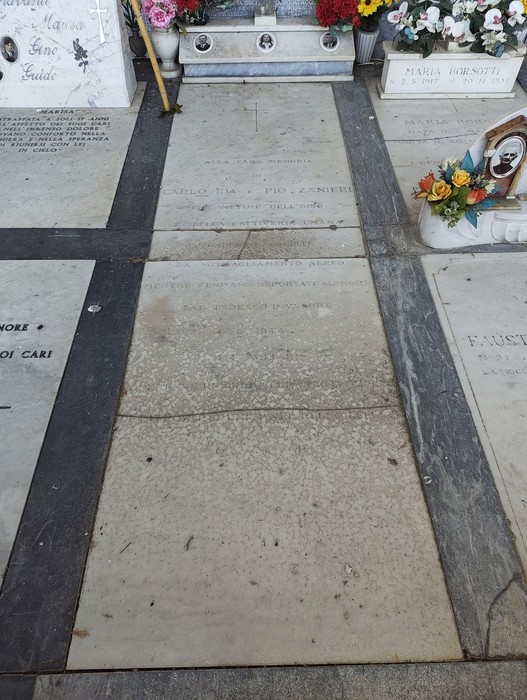Lastra tombale in marmo con iscrizione, tra altre sepolture in un cimitero.