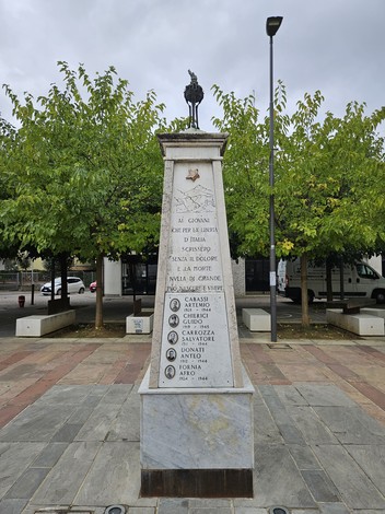 Monumento ai Partigiani, con iscrizioni commemorative e albero di castagno sullo sfondo. Atmosfera di ricordo e rispetto.