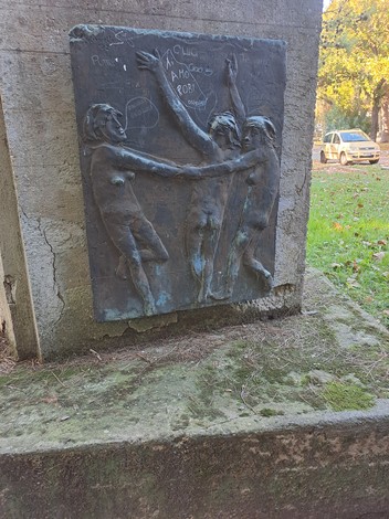 Monumento ai Caduti con rilievi di figure umane in atteggiamento di lotta, immerso nel verde.