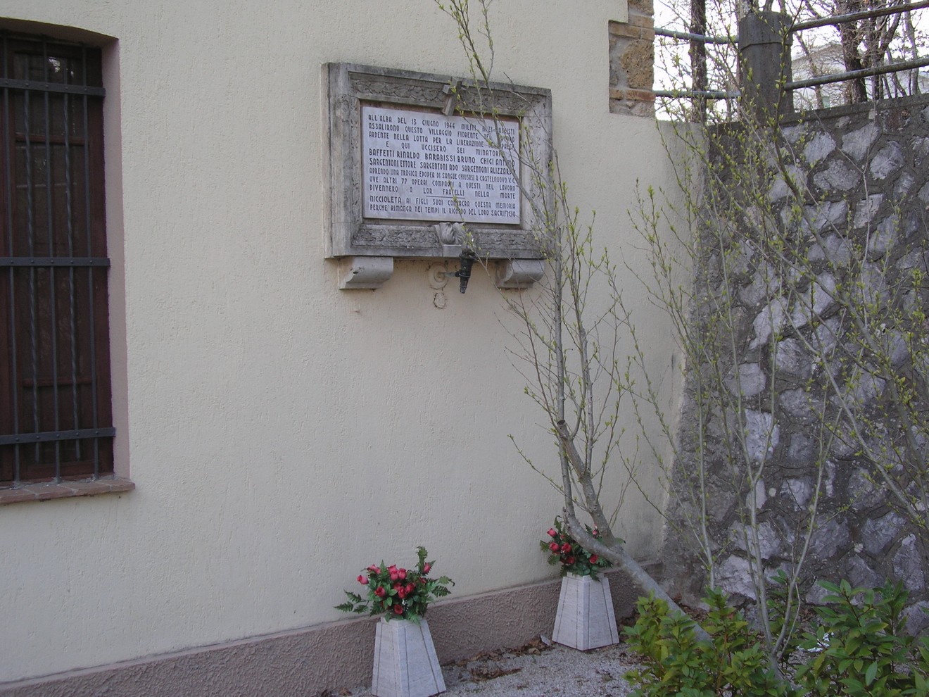 Lapide commemorativa di Niccioleta, situata su un muro con fiori ai piedi, in un contesto tranquillo.
