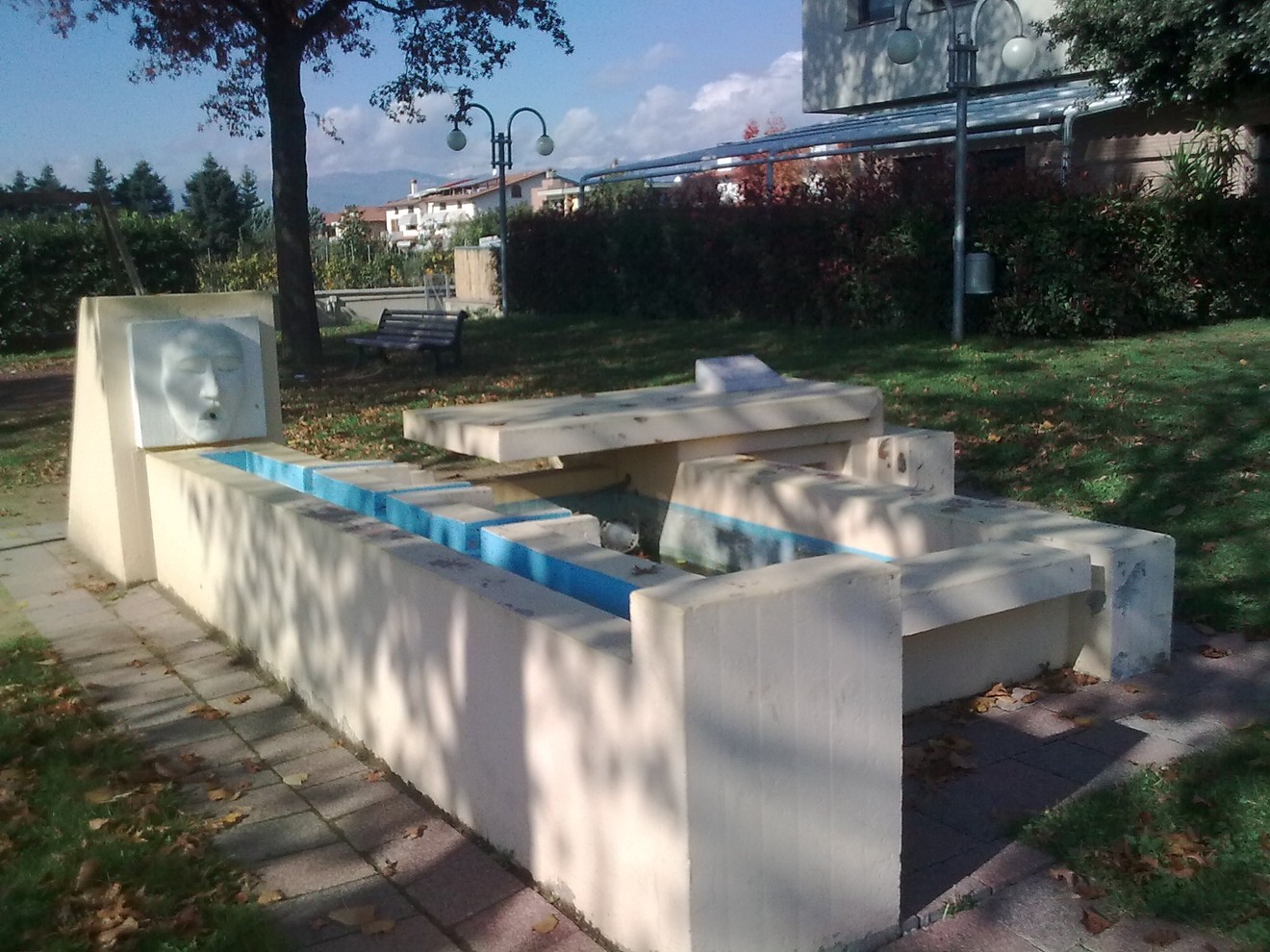 Fontana moderna in un parco, con elementi geometrici e un'architettura minimalista, circondata da vegetazione.