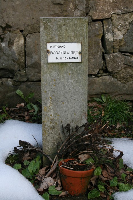 Targa commemorativa di un partigiano nel "Giardino dei caduti", circondata da vegetazione e neve.