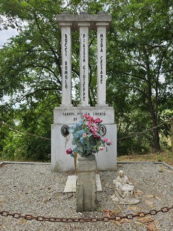 Cippo commemorativo con colonne, dedicato ai caduti per la libertà, decorato con fiori e statue.