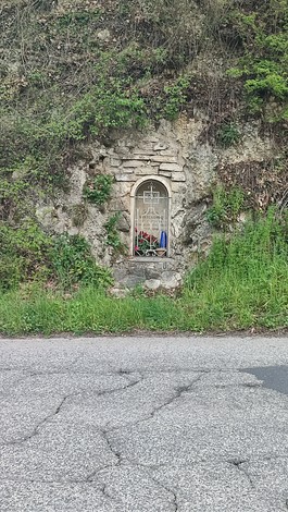 Edicola per Panichi incastonata nella roccia, circondata da vegetazione e fiori.