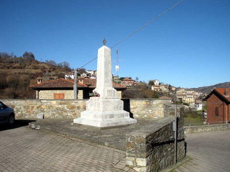 Monumento ai caduti di Romagnese, situato in un paesaggio collinare, circondato da abitazioni.