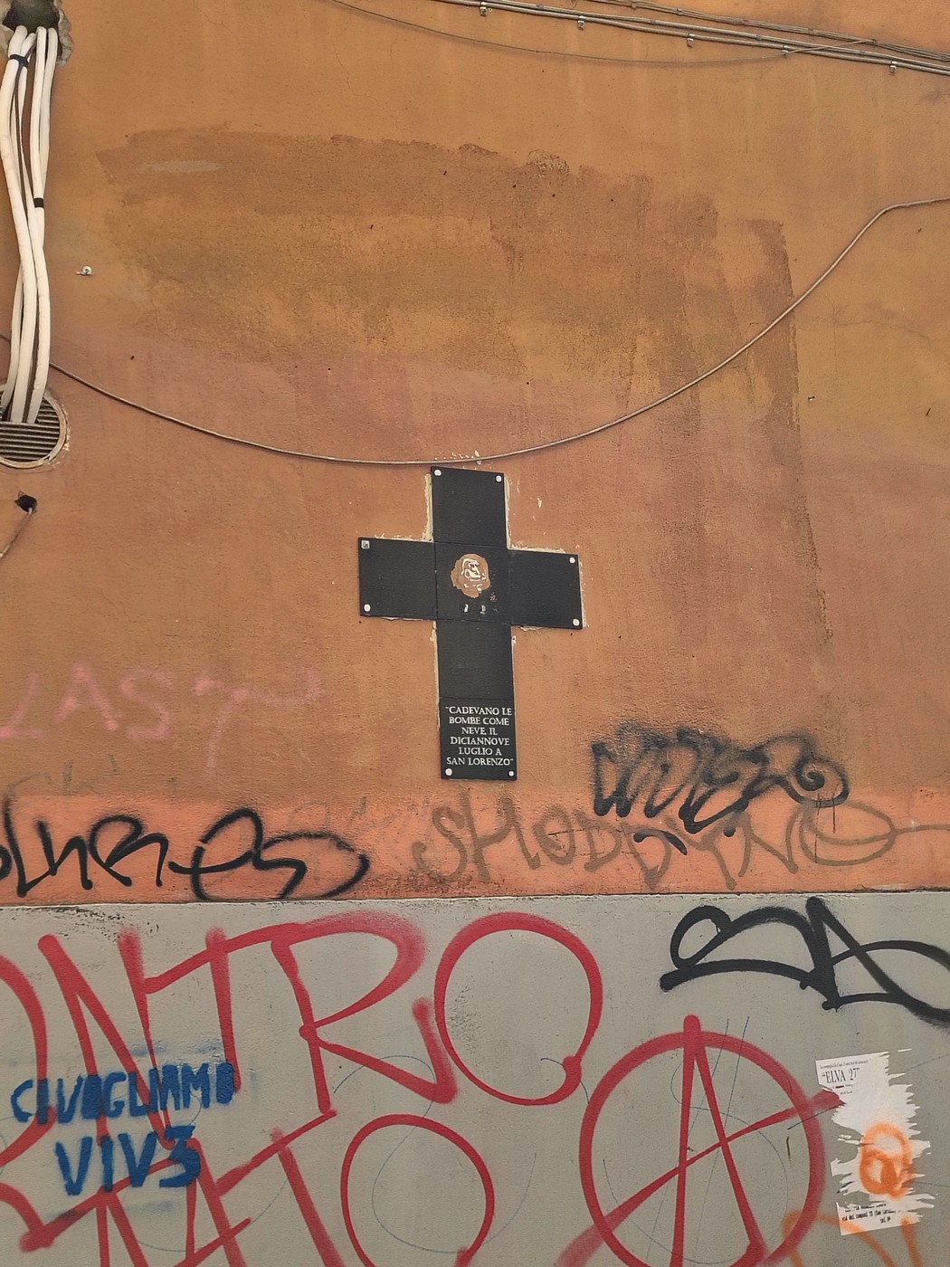 Croce commemorativa per i bombardamenti di San Lorenzo, collocata su una parete decorata da graffiti.