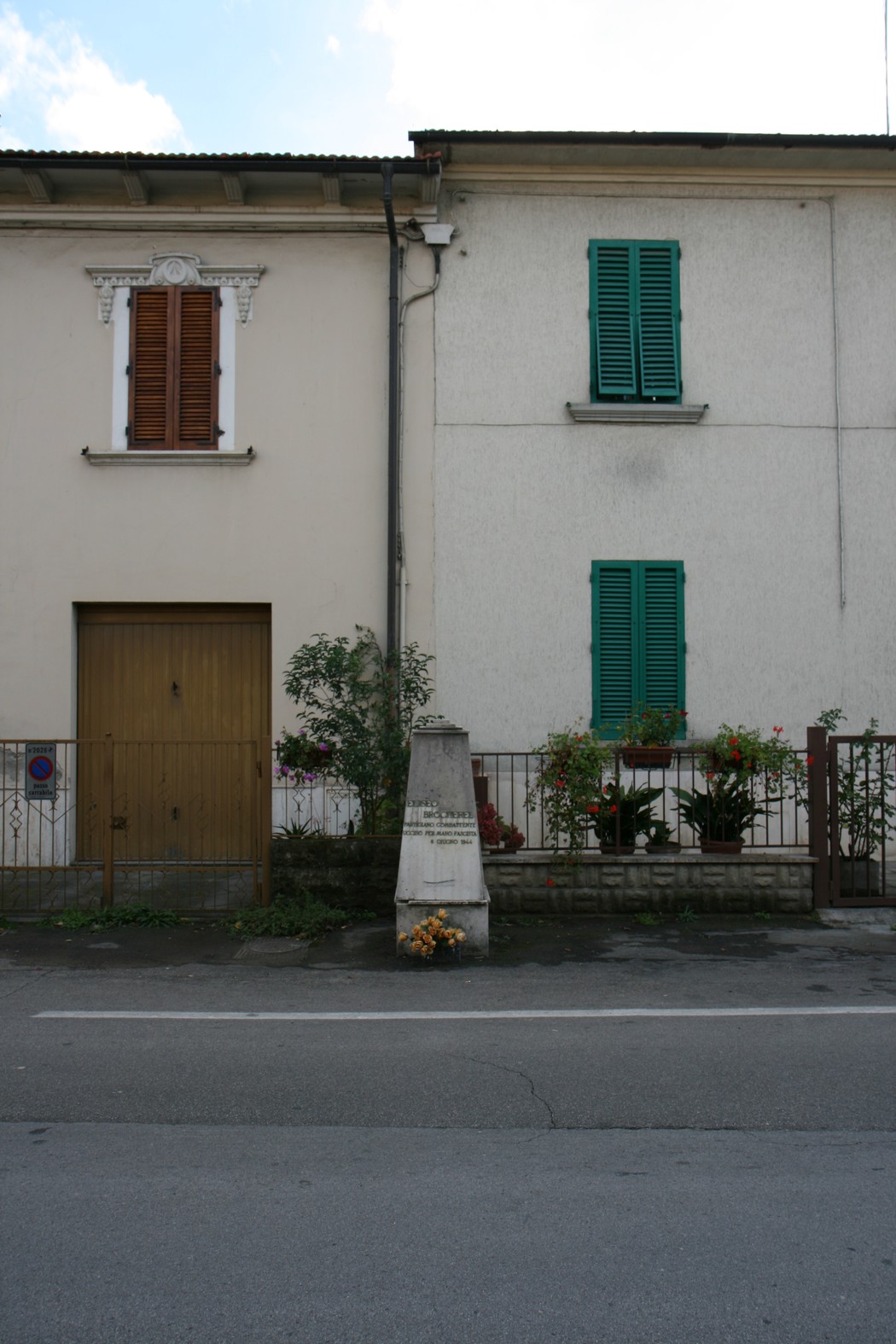 Cippo commemorativo a Brocherel, con case e fiori, rappresenta la memoria storica del luogo.