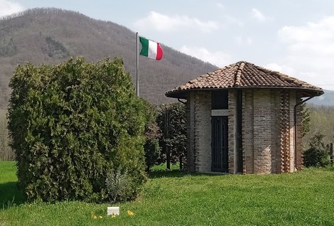 Sacrario dei martiri di Biagasco, un edificio circolare circondato da verde con bandiera italiana sullo sfondo.