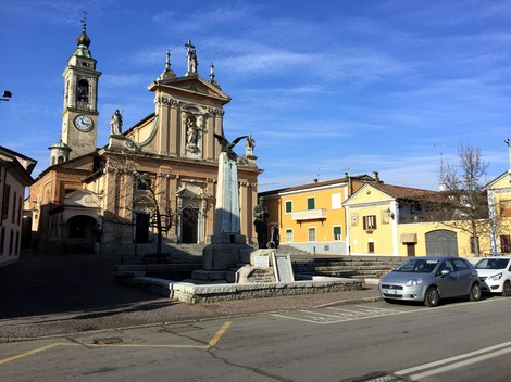Monumento ai Caduti di Gravellona Lomellina, ubicato in una piazza con chiesa e edifici colorati.