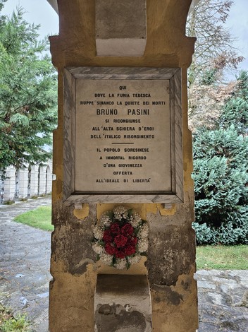 Lapide a Pasini, dedicata alla memoria di Bruno Pasini, situata in un contesto storico e verdeggiante.
