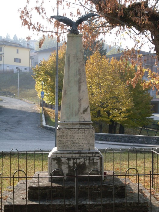 Monumento ai Caduti di Cavola, un obelisco con un'aquila, circondato da alberi e strade.
