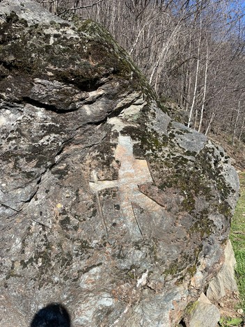 Roccia dei partigiani con incisioni storiche, circondata da vegetazione e alberi. Luce naturale e chiara.