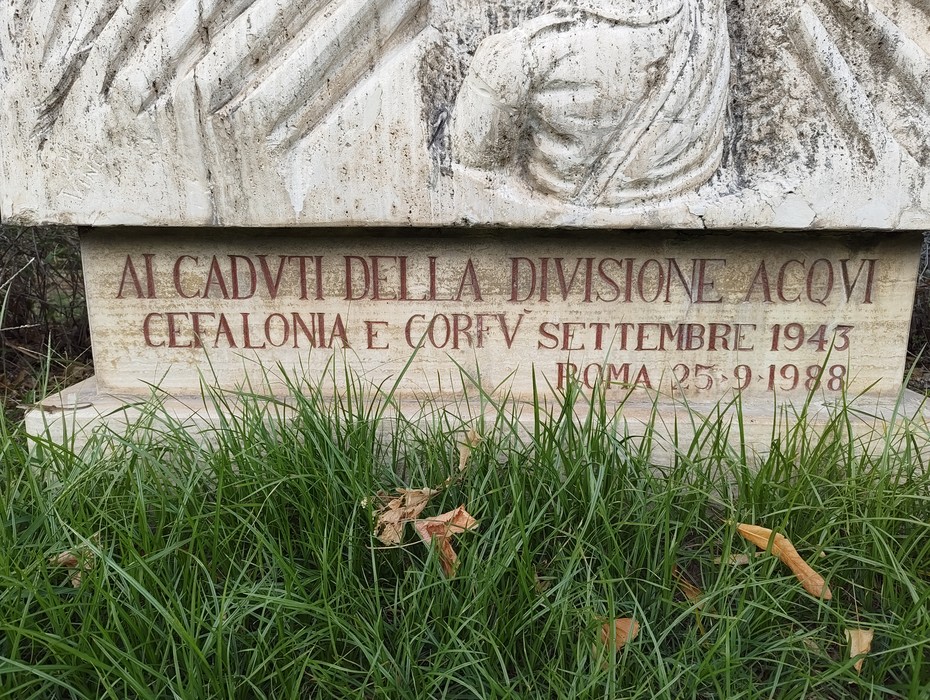 Monumento in pietra con rilievo scolpito e iscrizione, circondato dall’erba.