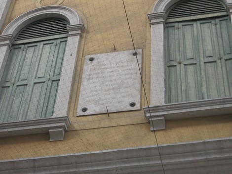 Lapide commemorativa sulla facciata del CLN di Mestre, con finestre verdi sullo sfondo.