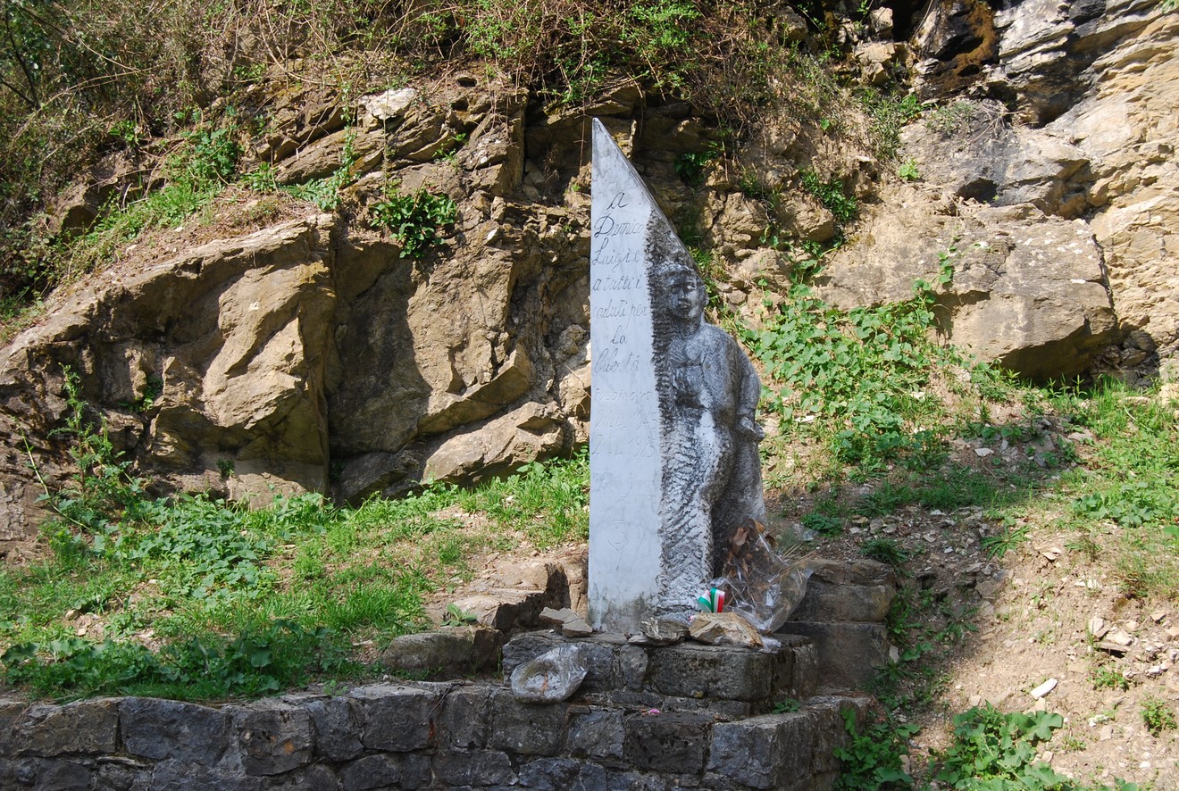 Monumento a Damico, eretto tra rocce e vegetazione, in memoria di una figura locale significativa.