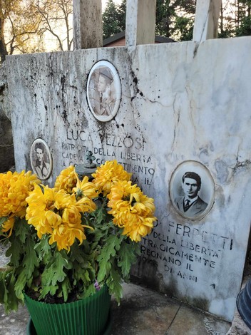 Monumento dedicato ai partigiani di Regnano, con fotografie commemorative e fiori gialli.