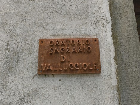 Insegna in bronzo che indica l'Oratorio di Vallucciole, immerso nella natura circostante.