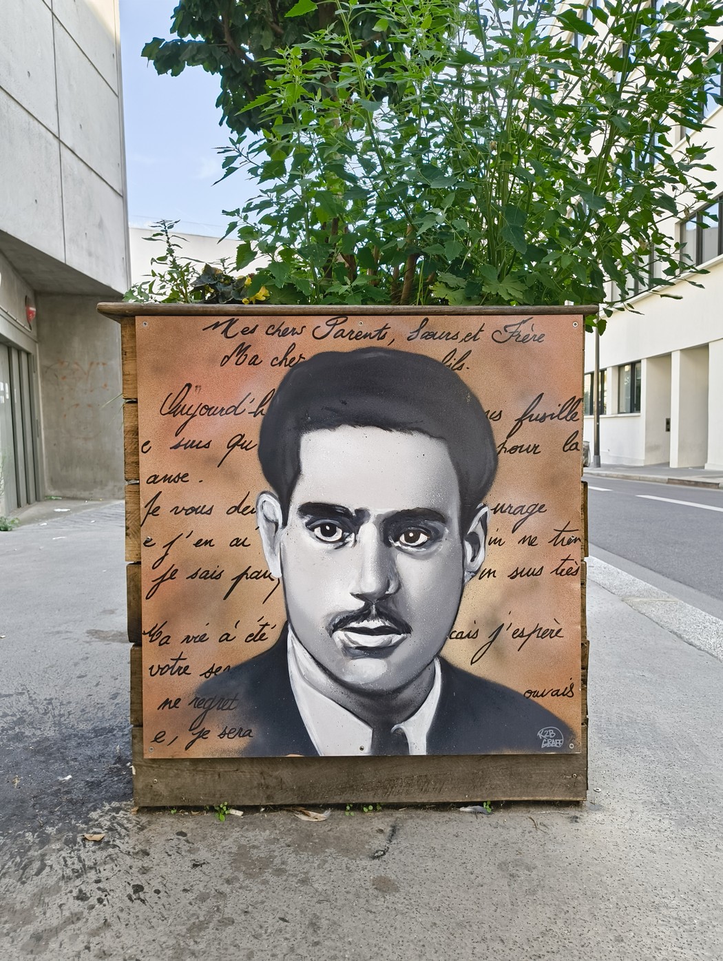 Ritratto di Manouchian con scritte commemorative su un muro in città, simbolo della resistenza.