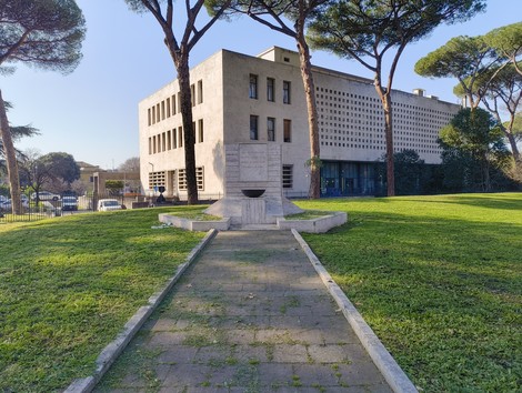 Monumento ai caduti militari, situato in un parco, circondato da alberi e vicinissimo a un edificio moderno.