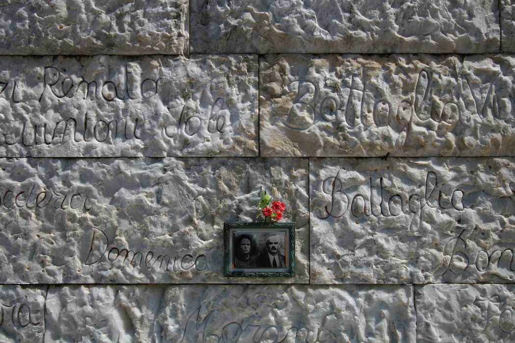 Sacrario delle vittime di Vinca, memoriale commemorativo con fotografie e nomi incisi su una parete di pietra.
