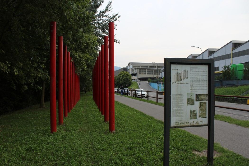 Memoriale del 29 gennaio 1945 con colonne rosse in un parco, circondato da vegetazione e un pannello informativo.