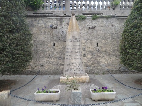 Monumento commemorativo dedicato a Valli ed altri, situato in un'area verde con fiori e alberi.