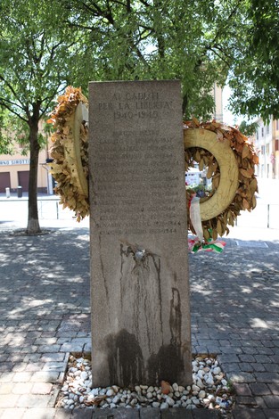 Monumento ai Caduti per la libertà, con una corona di fiori e un ambiente verdeggianti.