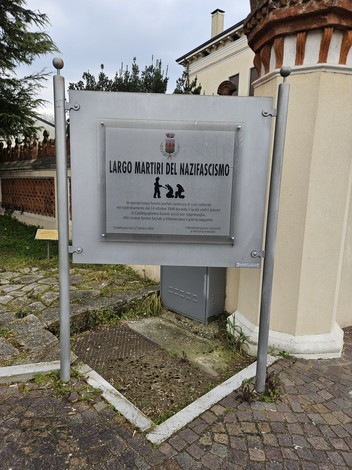 Insegna informativa di Largo Martiri del Nazifascismo, con dettagli architettonici circostanti e pavimentazione in pietra.
