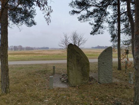 Monumento commemorativo in un paesaggio rurale, con due grandi pietre e alberi circostanti.