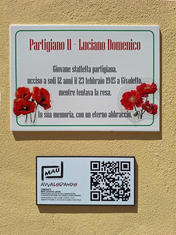 Murale dedicato a Luciano Domenico, partigiano, con fiori rossi e un codice QR, su sfondo giallo.