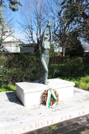 Monumento alla 63° Brigata Garibaldi con statua commemorativa e corona di fiori, immerso nel verde.
