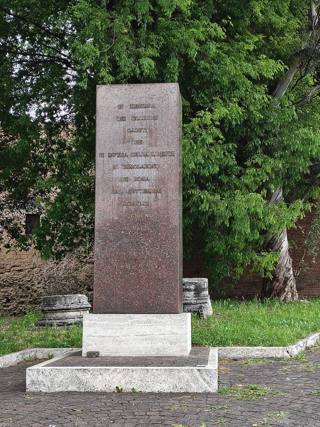Monumento ai caduti per la Libertà, con una struttura in pietra circondata da verde e elementi architettonici.