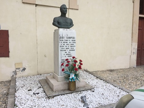 Monumento dedicato a Gigi Campegi, con busto e decorazioni floreali, ubicato in un'area storica.