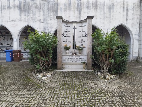 Sacrario dei deportati con monumento commemorativo circondato da vegetazione e muretti in un contesto sobrio e rispettoso.