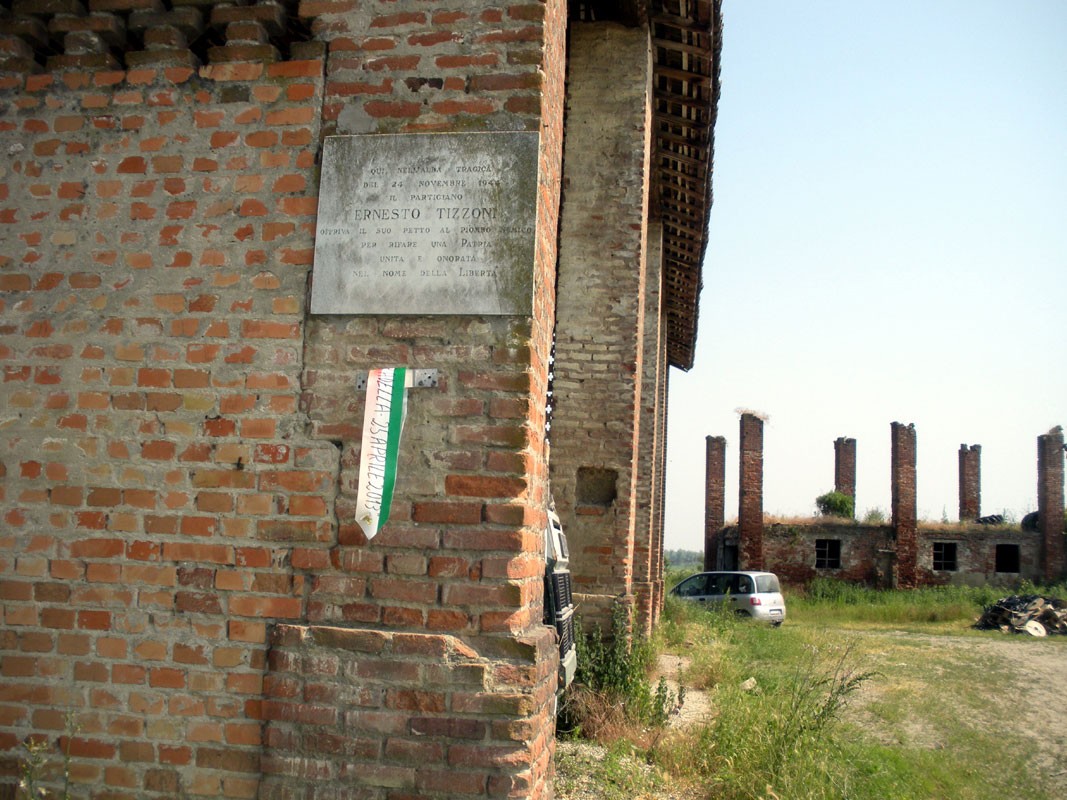 Lapide commemorativa dedicata a Ernesto Tizzoni in un'area storica con resti di edifici in mattoni.