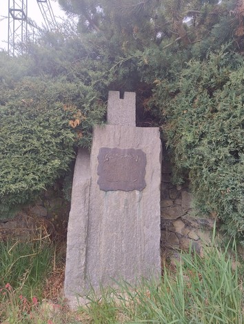 Cippo commemorativo dedicato alle popolazioni montane, circondato da vegetazione.