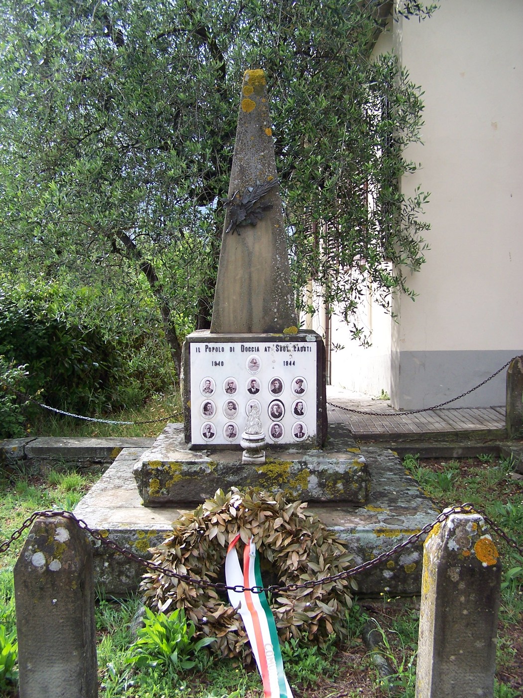 Cippo commemorativo di Doccia, dedicato ai caduti, con foto e ghirlanda di alloro ai piedi.