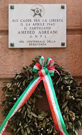 Lapide commemorativa dedicata al partigiano Amedeo Andreani, decorata con una corona di alloro e nastri tricolori.
