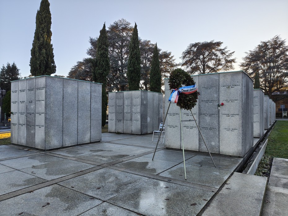 Campo della Gloria con monumenti funerari e una corona di fiori, circondato da alberi e cielo sereno.