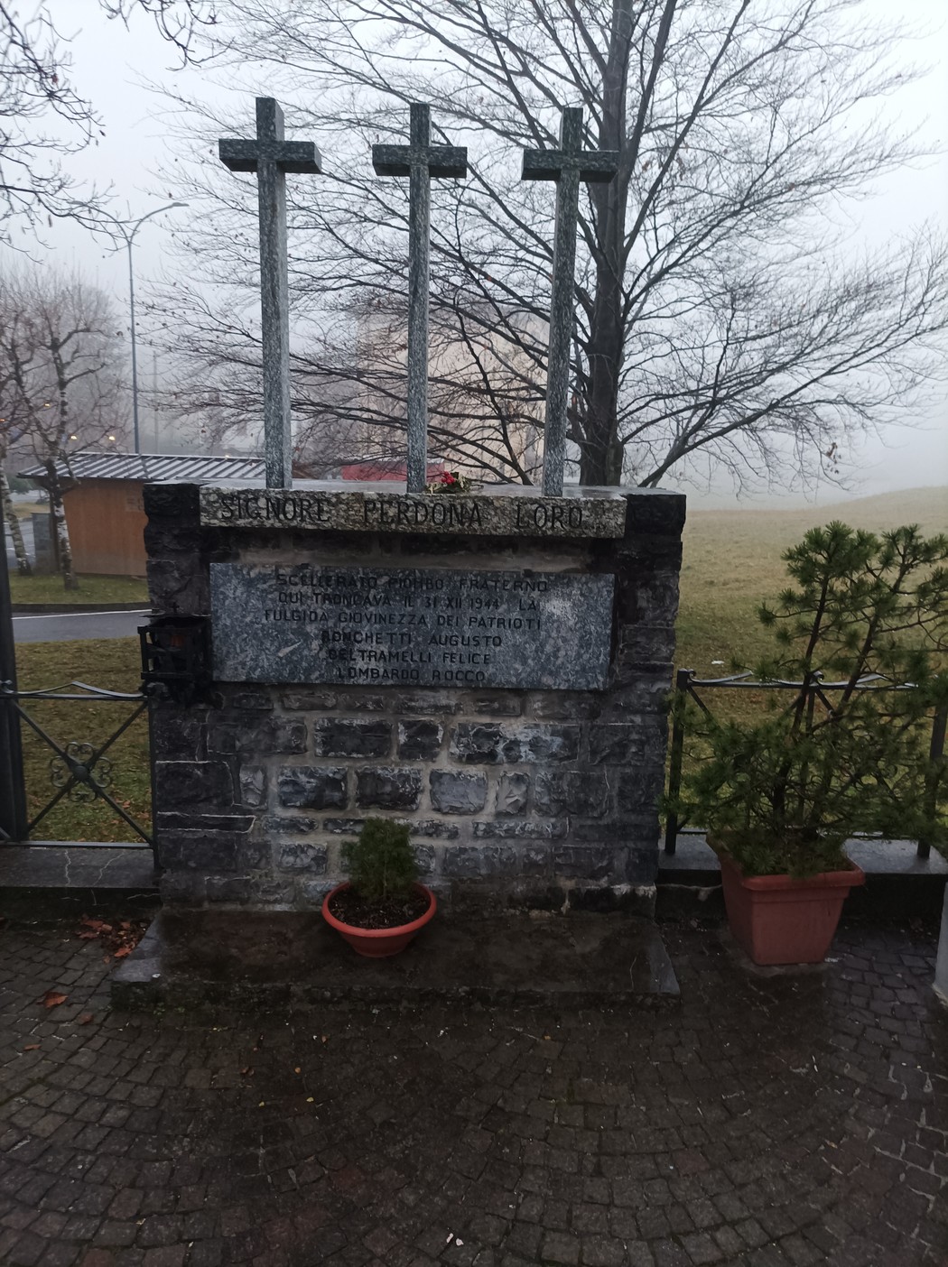 Monumento in memoria di Bonchetti, Beltramelli e Lombardo, con tre croci, situato in un contesto nebbioso.