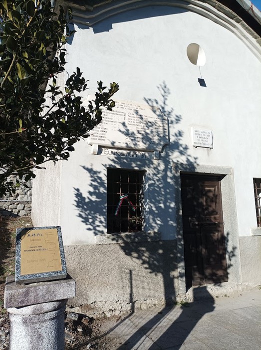 Lapide dedicata ai caduti partigiani, situata su un edificio bianco con ombre proiettate sul muro.