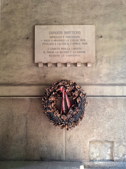 Lapide commemorativa in onore di Donato Bottero, con una corona di fiori sotto.