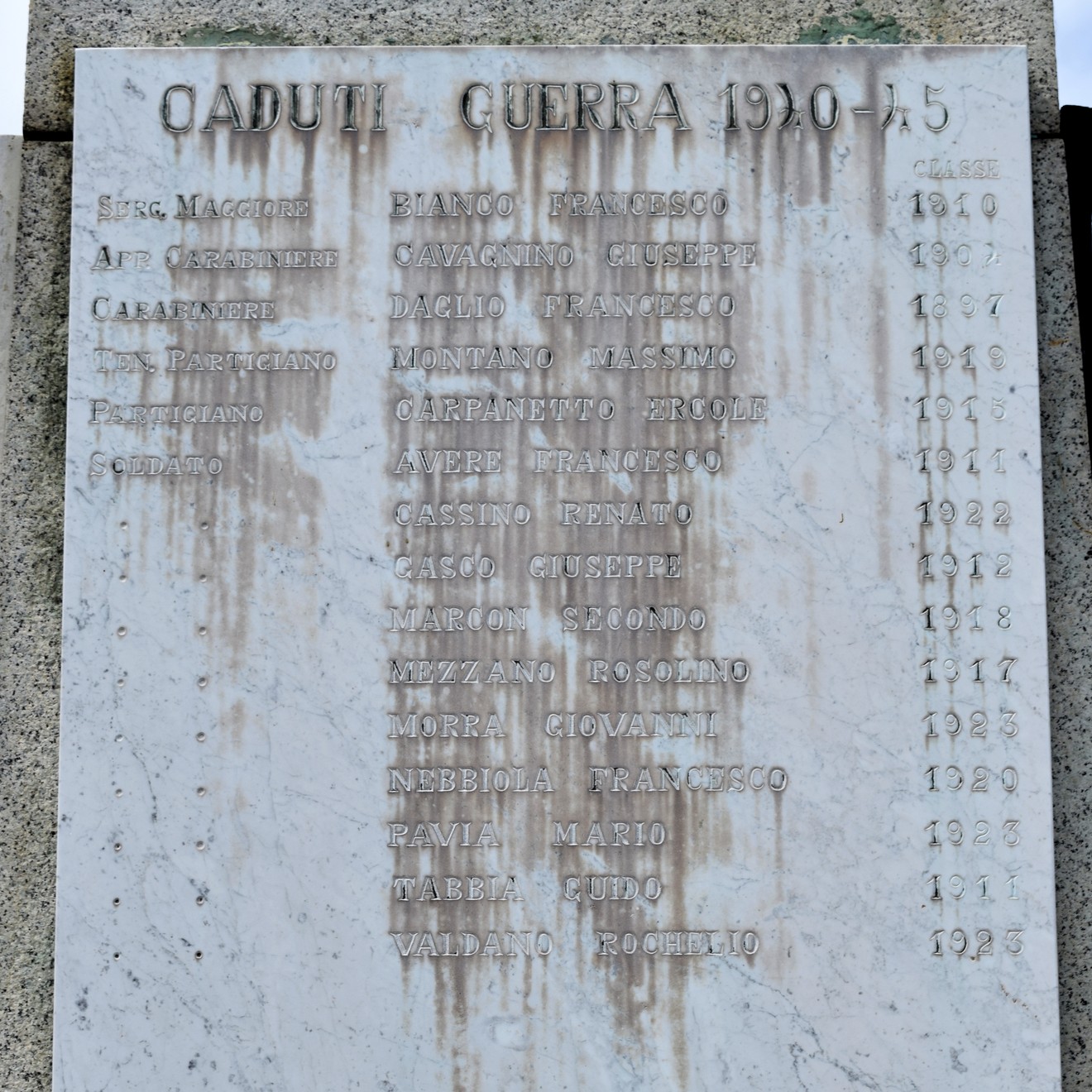 Lapide in pietra con iscrizione ai caduti della guerra, fissata su una parete.