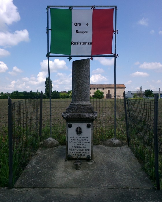 Cippo commemorativo dedicato a Pietro Battini, simbolo di resistenza e libertà, circondato da un paesaggio rurale.