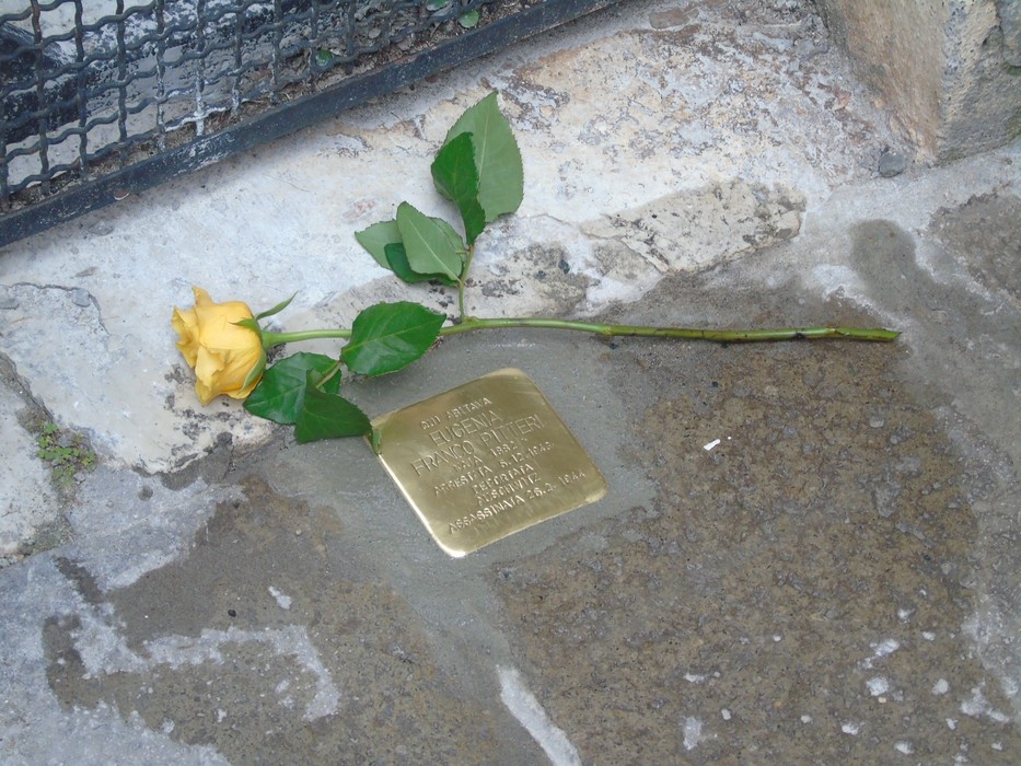 Pietra d'inciampo con una rosa gialla posata accanto, in memoria di Franco e Foà.