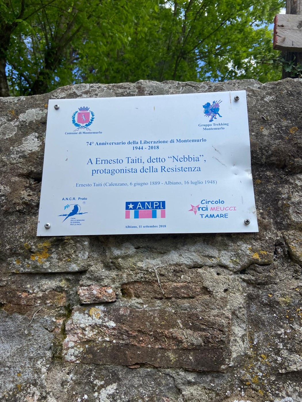 Targa commemorativa dedicata a Ernesto Taiti, protagonista della Resistenza, affissa su un muro in un contesto naturale.