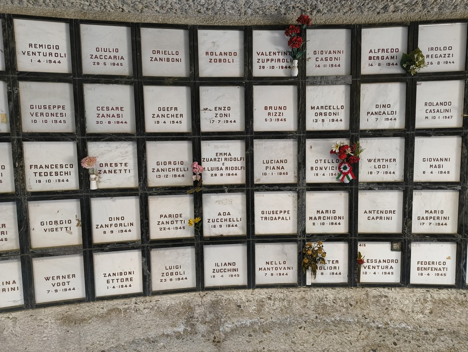 Monumento Ossario dedicato ai caduti partigiani, con lastre commemorative e fiori in ricordo.