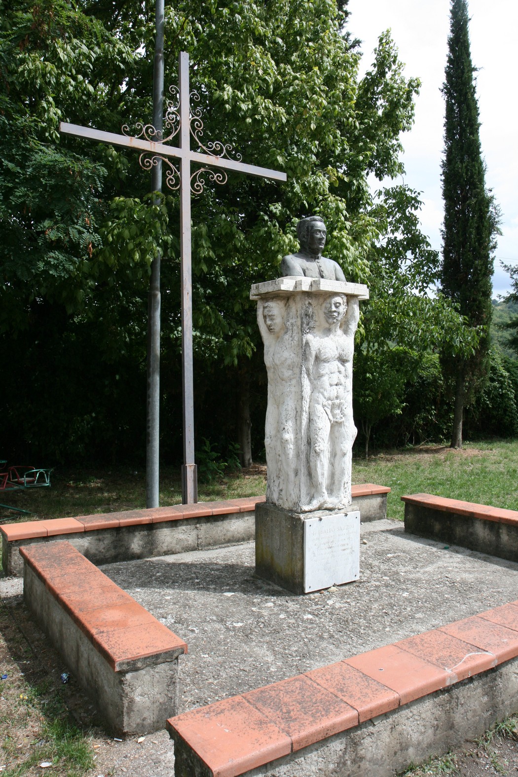 Monumento a Don Sazzini, con statue e croce, immerso in un verdeggiante contesto naturale.
